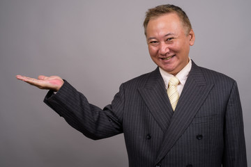 Portrait of mature Asian businessman against gray background