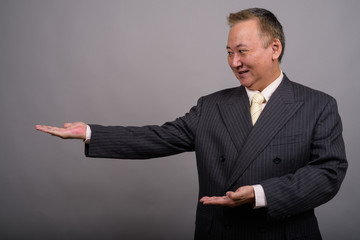 Portrait of mature Asian businessman against gray background