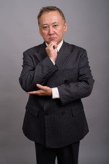 Portrait of mature Asian businessman against gray background