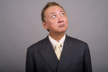 Portrait of mature Asian businessman against gray background