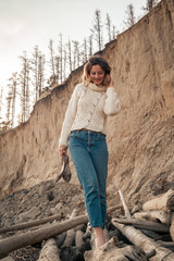 Naklejka premium Atmospheric lifestyle photo of young beautiful woman white knit sweater made of natural wool and jeans in on the beach.The concept of the unity of women and nature, peaceful mood, eco-friendly life