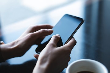 Close up of women's hands holding smartphone, female using mobile phone during coffee break.