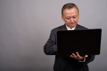 Portrait of mature Asian businessman against gray background