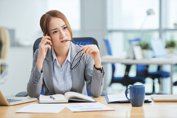 Young pensive businesswoman sitting at office desk with notepad and thinking about new business project at office