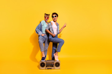 Full length body size view photo student leg touch boom box gesture v-sign summer journey weekend travel wavy curly beautiful trendy style stylish t-shirt jeans top-knot isolated yellow background 