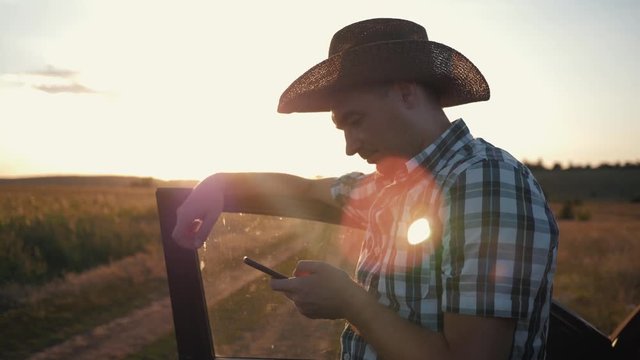 A man-farmer is wearing a hat at sunset and is working on a smarphone. Communication with customers. Modern business with innovative technologies. Online sales and purchases