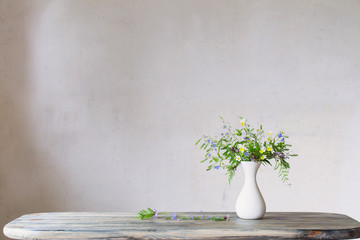 wildflowers in white vase on background old wall