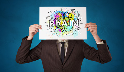 Young person holding white paper in front of her head with colorful brain concept
