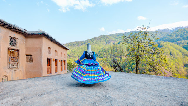 Woman dressed in colorful traditional clothes in the background Masuleh village houses - Gilan province - Iran