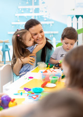Teacher with group of kids working with plasticine at kindergarten or playschool
