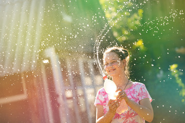joyful girl playing with splashes and streams of water. fantastically beautiful on a green background with colorful highlights, in the summer in the village