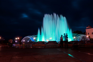 Big illuminated fountain at night in a city with people's silhouettes