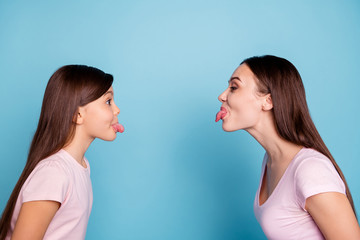 Close-up profile side view portrait of two nice attractive charming foolish childish cheerful straight-haired girls showing tongue out isolated over bright vivid shine green blue turquoise background