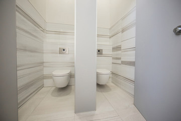 A pair of toilet cubicles in an office building made in marble and wood