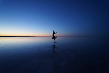Jumping silhouette reflection over a salt lake at blue hour