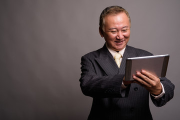 Portrait of mature Asian businessman against gray background