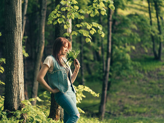 Cute Caucasian young woman with a bouquet of lilies of the valley in the forest