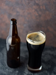 Craft beer porter poured into a glass from a bottle on a concrete dark background