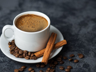 White espresso coffee Cup with cinnamon and coffee beans on dark concrete background
