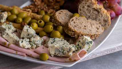 Wine snacks set. Blue cheese, Mediterranean olives, baguette slices, grissini, ham, grapes and different nuts on the plate. Tasty wine appetizer background. Copy space