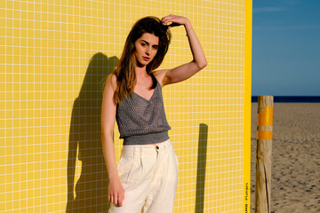 a young model with long hair in front of a yellow wall in a summer day