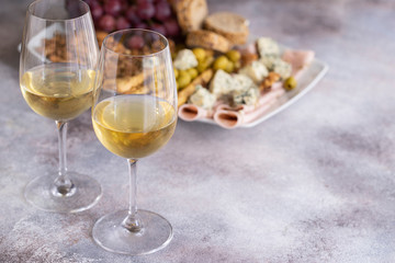 Two glasses of white wine and plate with different snacks. Blue cheese, olives, baguette slices, grissini, ham, grapes and nuts. Wine snacks set background.Copy space