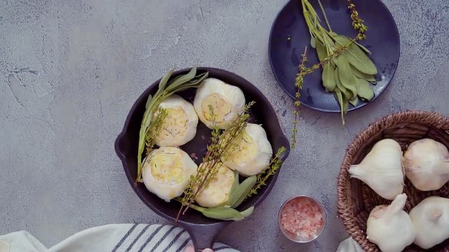 Raw garlic heads with fresh spices in cast iron skillet for preparing roasted garlic recipe.
