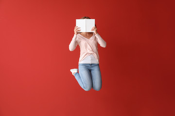 Jumping young woman with book on color background