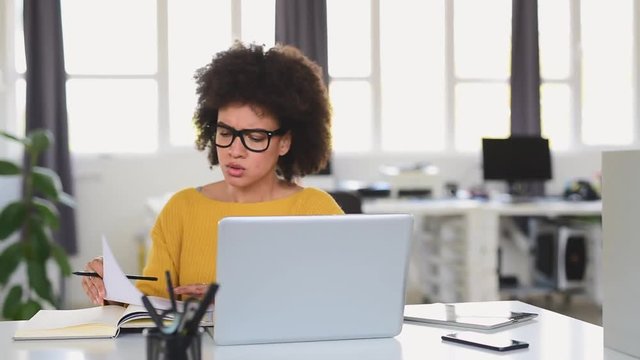 Charming mixed race businesswoman sitting in modern office and using laptop.