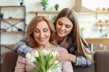 Happy daughter and her mother with bouquet of flowers at home