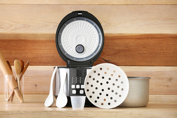 Modern multi cooker with accessories on table against wooden background