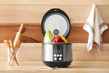 Modern multi cooker with vegetables on kitchen table