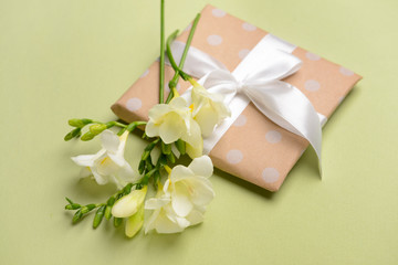 Fototapeta na wymiar Beautiful freesia flowers and gift on color background