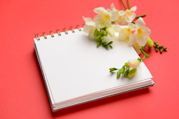 Beautiful freesia flowers and notebook on color background