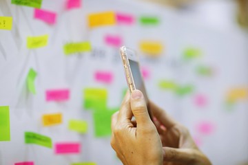 People hand holding smartphone on whiteboard and colors paper noted blur background