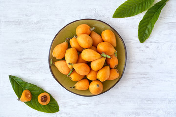 Loquat fruit. Nispero. Eriobotrya Japonica. Loquat in plate with fresh leaves on wood background	