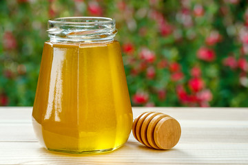 Jar of organic floral honey with a drizzle against flowers background . Outdoor.	