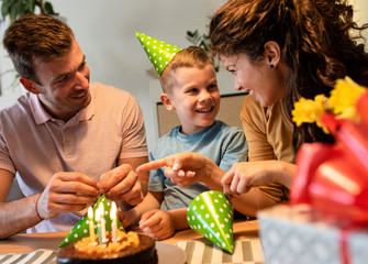 Happy family celebrating a birthday together at home.Young parents with son preparing birthday cap.