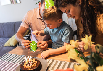 Happy family celebrating a birthday together at home.Young parents with son preparing birthday cap.