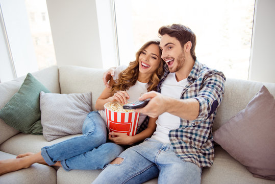 Portrait of his he her she two person nice attractive lovely charming cheerful guy lady spending time sitting on divan watching hilarious funny movie in light white style interior living room house