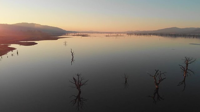Smooth still lake at sunset showing wide vista with tree reflections. aerial drone footage. Hume Weir