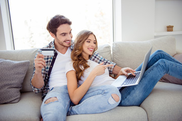 Portrait of her she his he two person nice attractive lovely cheerful cheery guy lady sitting oncozy  divan showing options buying goods on web site in light white style interior living room
