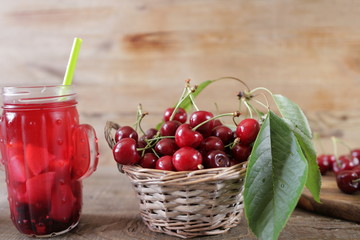 fresh sweet cherry in a straw basket with a smoothie in a glass beaker on a wooden background