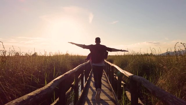 Ragazzo corre in libert&agrave; con le braccia aperte tipo aeroplano su un ponte di legno in mezzo alle piante.