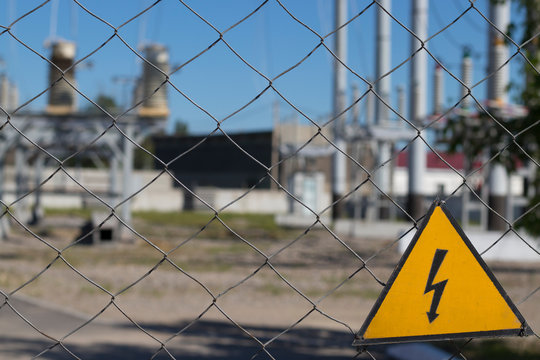 Electrical hazard sign on metal grid. On the background of unfocused high-voltage electrical substation. Concept: danger of electric current, death from electric shock