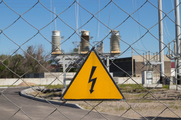 Electrical hazard sign on metal grid. On the background of unfocused high-voltage electrical substation. Concept: danger of electric current, death from electric shock