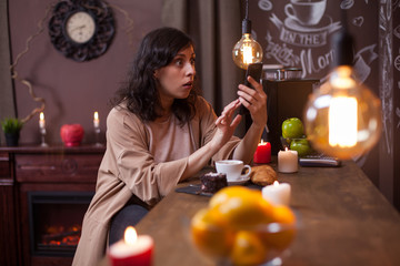 Portrait of shocked young woman sitting at a bar counter in a coffee shop looking at her phone