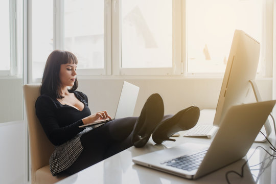 lateral view of a hot brunete in office outfit sitting on the floor and working on computer