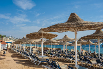 Thatched beach umbrellas and loungers on a beach at an idyllic tropical resort for a summer vacation