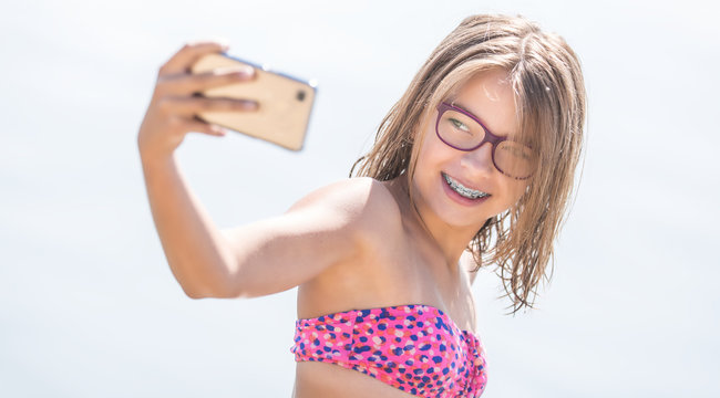 Happy young girl with dental braces making selfhie on beach in summer hot day